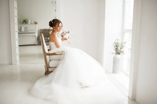 Joven novia en un vestido de lujo sosteniendo un ramo de flores en un estudio de color blanco brillante. concepto de moda de boda . — Foto de Stock