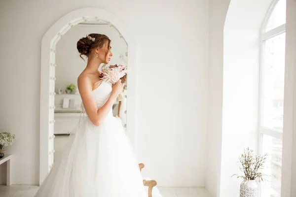 Молода наречена в розкішній сукні тримає букет квітів у яскраво-білій студії. концепція весільної моди . — стокове фото