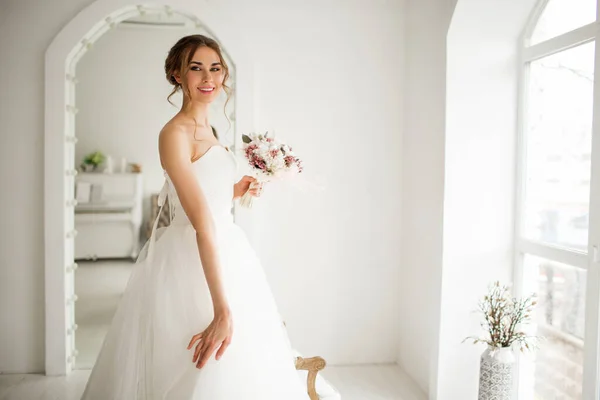 Noiva jovem em um vestido de luxo segurando um buquê de flores em estúdio branco brilhante. Conceito de moda casamento . — Fotografia de Stock