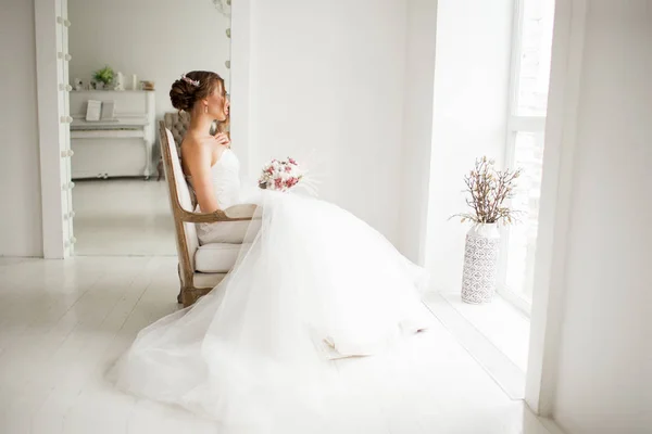 Lüks elbiseli genç gelin parlak beyaz stüdyoda bir buket çiçek tutuyor. Düğün moda konsepti. — Stok fotoğraf