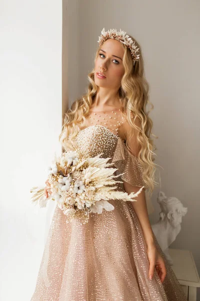 Νεαρή νύφη με ένα όμορφο φόρεμα και στεφάνι στο κεφάλι κρατώντας ένα μπουκέτο λουλούδια σε φωτεινό λευκό στούντιο. Έννοια γάμου. — Φωτογραφία Αρχείου