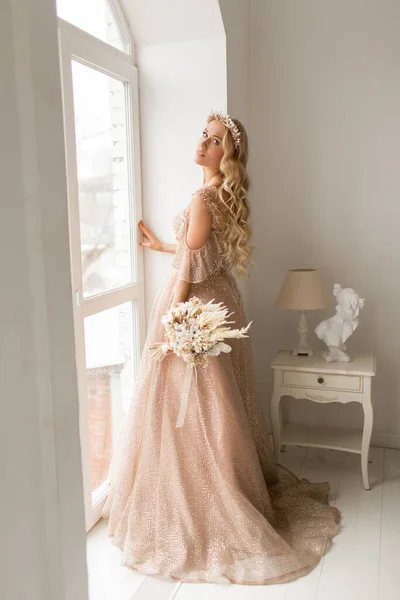 Joven novia en un hermoso vestido y corona en su cabeza sosteniendo un ramo de flores en un estudio de color blanco brillante. Concepto de boda . — Foto de Stock
