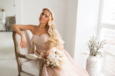 Güzel elbiseli ve kafasında çelenk olan genç gelin parlak beyaz stüdyoda bir buket çiçek tutuyor. Düğün konsepti.