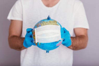 Adam dünyayı tıbbi maskenin içinde tutuyor. Covid-19 konsepti.