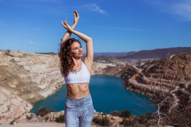 Genç zayıf kadın dağ gölünde yoga yapıyor.