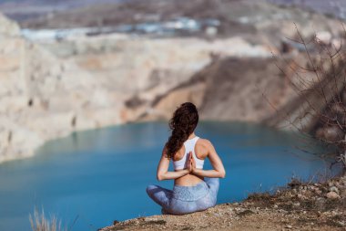 Genç zayıf kadın dağ gölünde yoga yapıyor.