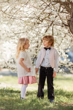 Mutlu küçük kız ve erkek kardeş açık havada kiraz bahçesinde oynuyorlar. Bahar geldi..