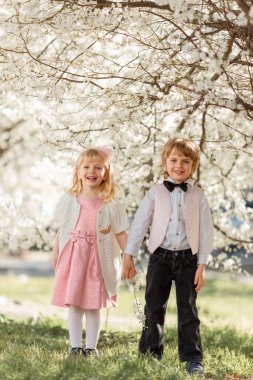 Mutlu küçük kız ve erkek kardeş açık havada kiraz bahçesinde oynuyorlar. Bahar geldi..