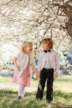 Mutlu küçük kız ve erkek kardeş açık havada kiraz bahçesinde oynuyorlar. Bahar geldi..