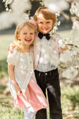 Mutlu küçük kız ve erkek kardeş açık havada kiraz bahçesinde oynuyorlar. Bahar geldi..