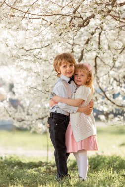 Mutlu küçük kız ve erkek kardeş açık havada kiraz bahçesinde oynuyorlar. Bahar geldi..