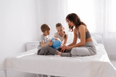 Mutlu aile annesi, kızı ve oğlu beyaz yatak odasında eğleniyor. Evde kalıp konsept yapın..