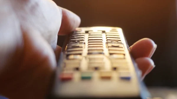 Close up of womans hand with a television remote control changing channels at sunset time