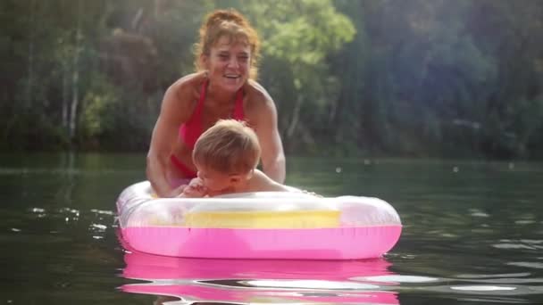 Little baby and grandma swimming in a lake on inflatable mattress in