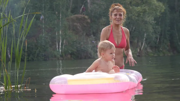 Little baby with grandma swimming on inflatable mattress in a lake in sunny day in summer