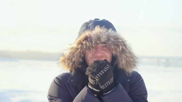 Portrait of young man outdoors freezes looking into the camera warms your hands in winter on sunny day