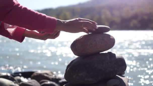 Female hands putting pebble stack next to the mountain river in slow motion. 3840x2160