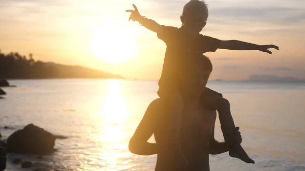 Dad keeps on his hands and throws son at amazing sunset on tropical beach.