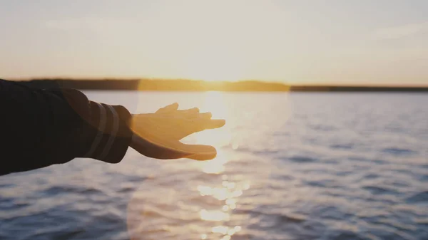 Close up of male hand at sunset on sea. Mans hand in suns rays on background sea water in nature. summer time glare of sun through fingers.