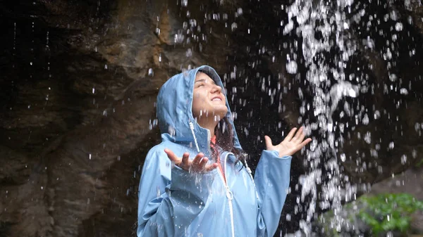 Young happy woman arms outstretched behind spectacular waterfall. Young woman outstretching arms by majestic waterfall.