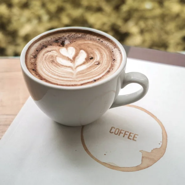 Una taza de café latte arte con el corazón en una taza blanca en un libro de — Foto de Stock