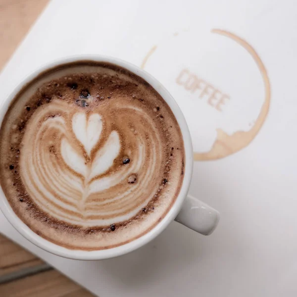 Una taza de café latte arte con el corazón en una taza blanca en un libro de — Foto de Stock