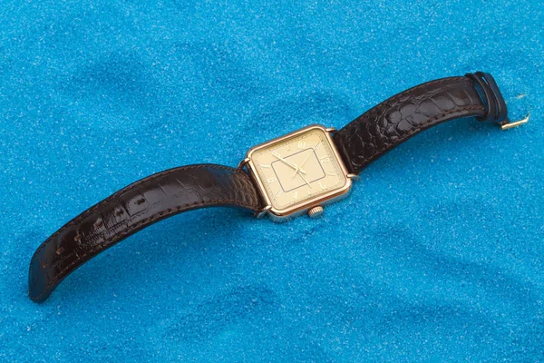 Золотые наручные часы на голубом песке — стоковое фото