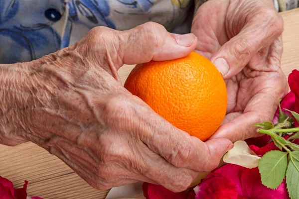 Mãos de uma velha com uma laranja — Fotografia de Stock