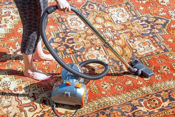 Woman vacuums an old carpet — Stock Photo, Image