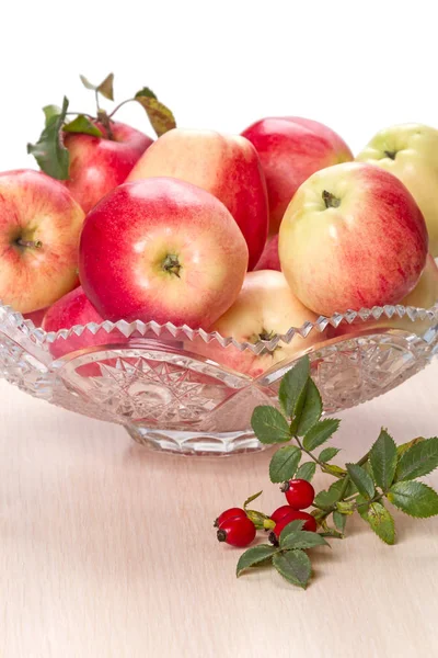 Manzanas maduras en un jarrón de cristal y rosa mosqueta — Foto de Stock