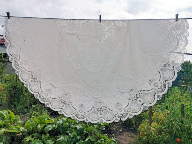 Beyaz dantelli masa örtüsü sokakta kurumuş.