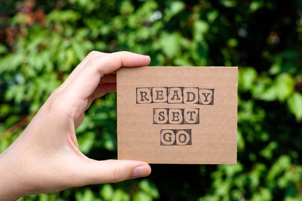 Woman hand holding cardboard card with words Ready Set Go