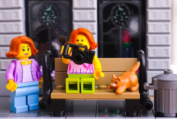 Девочка из Lego с фотоаппаратом и кошкой, сидящей на скамейке на улице — стоковое фото