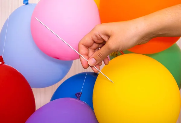 Woman hand with knitting needle ready to pop a yellow balloon