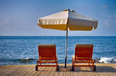 Şemsiye ve deniz sahilde iki şezlong