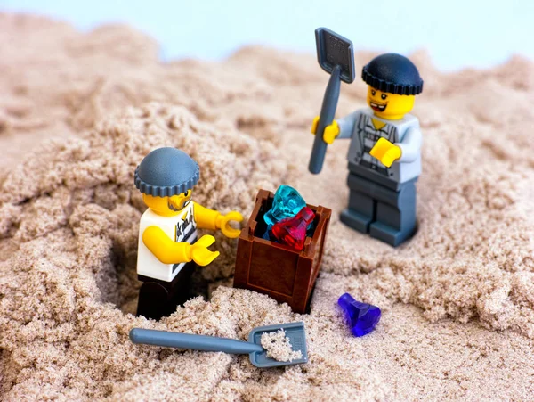 Two Lego robbers digging out box with gems from sand — Stock Photo, Image