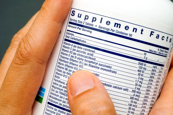 White plastic jar with supplement facts of multivitamins in hands — Stock Photo, Image