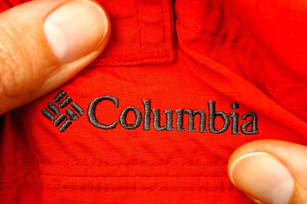 Wyszywane logo Columbia na czerwone ubrania w ręce kobiety. — Zdjęcie stockowe