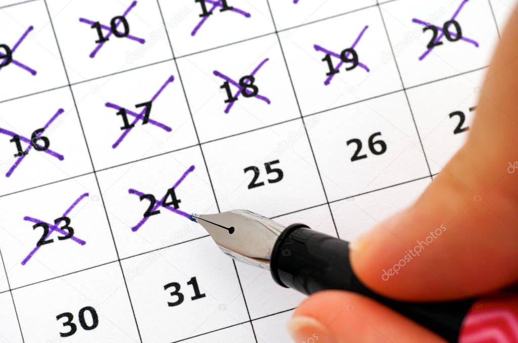 Fountain pen in woman hand marking days in calendar. 