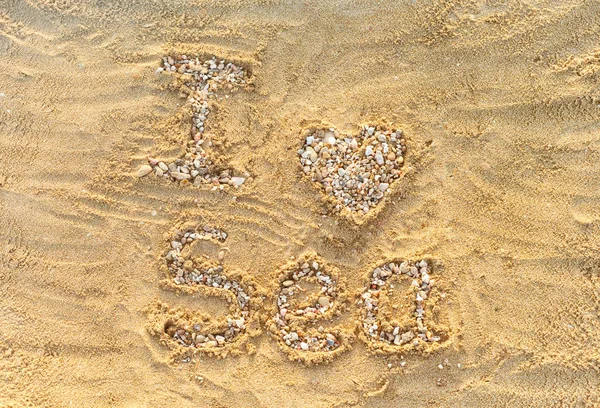 Adoro il mare. Lettere e cuore fatti da piccole pietre e conchiglia — Foto Stock