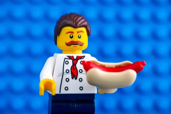 Lego chef com cachorro-quente contra fundo placa de base azul — Fotografia de Stock