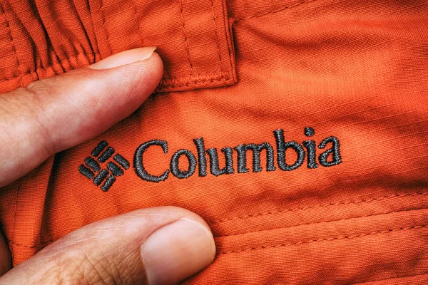 Wyszywane logo Columbia na czerwone ubrania między osoba palce. — Zdjęcie stockowe