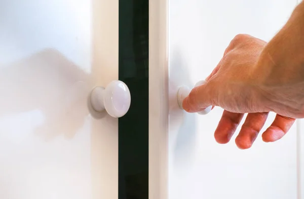 Person hand opening door of white wardrobe.