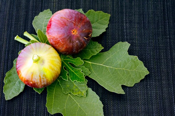 Two organic figs with leaves on black bamboo napkin — Stock Photo, Image