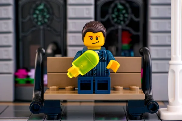 Lego-Geschäftsmann isst Eis auf der Bank draußen. — Stockfoto