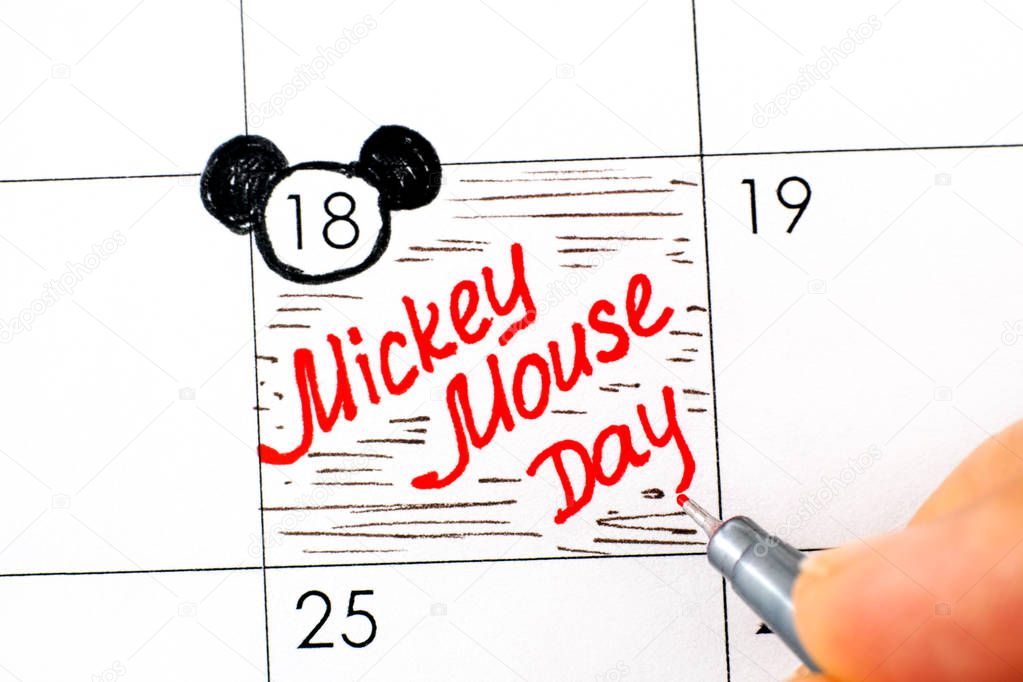 Woman fingers with pen writing reminder Mickey Mouse Day in cale