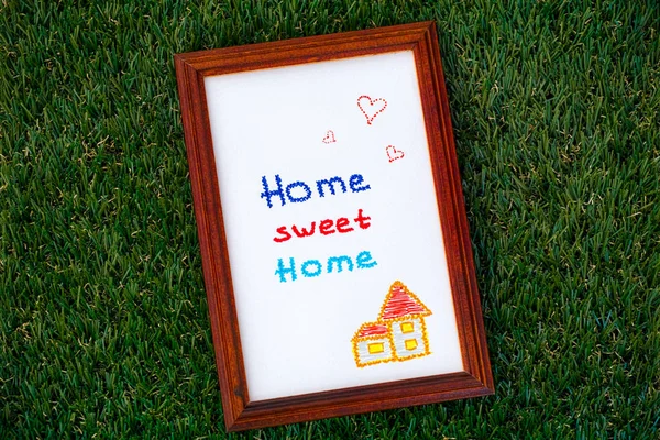 Home sweet home picture in wooden frame on grass background.