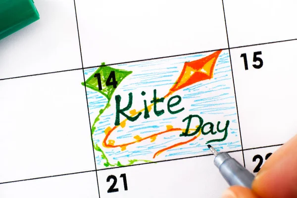 Dedos de mulher com caneta escrevendo lembrete Kite Day no calendário . — Fotografia de Stock