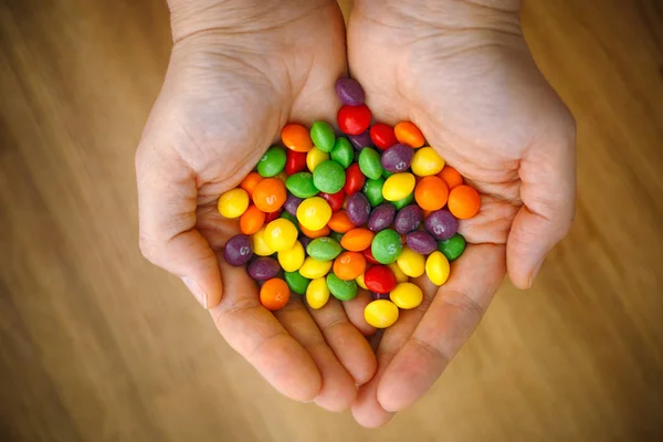 Skittles çok renkli meyveli şekerler kadınların elinde. Tahta sırt. — Stok fotoğraf