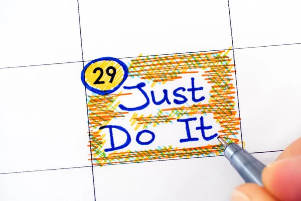 Vrouw vingers met pen schrijven herinnering Just Do It in kalender. — Stockfoto